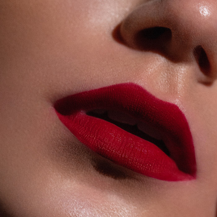 Matowa pomadka Hedonista Devil Wears Red Lipstick – intensywny, chłodny czerwony odcień na ustach modelki