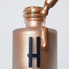 Płynny rozświetlacz Hedonista w złotym odcieniu – butelka z aplikatorem i metaliczna formuła