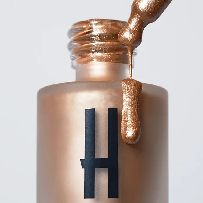 Płynny rozświetlacz Hedonista w złotym odcieniu – butelka z aplikatorem i metaliczna formuła